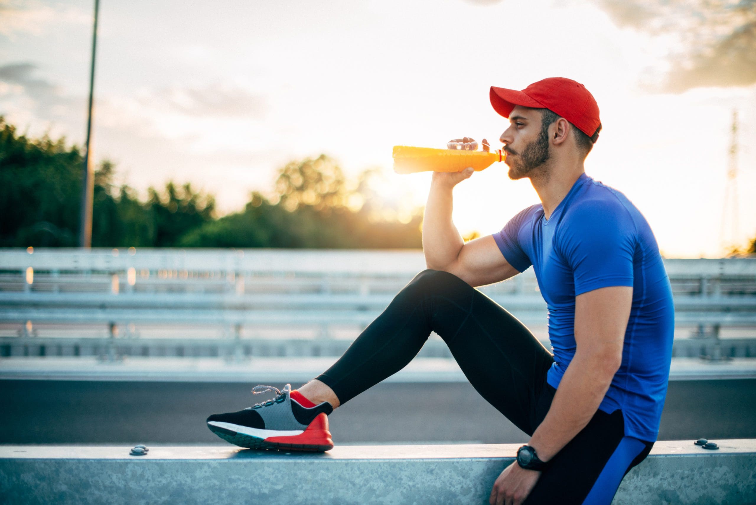 Image of young muscular male doing exercises outdoors on summer day, keeping body in fit shape and drinking Freshly squeezed citrus juices  to refuel and rehydrate.