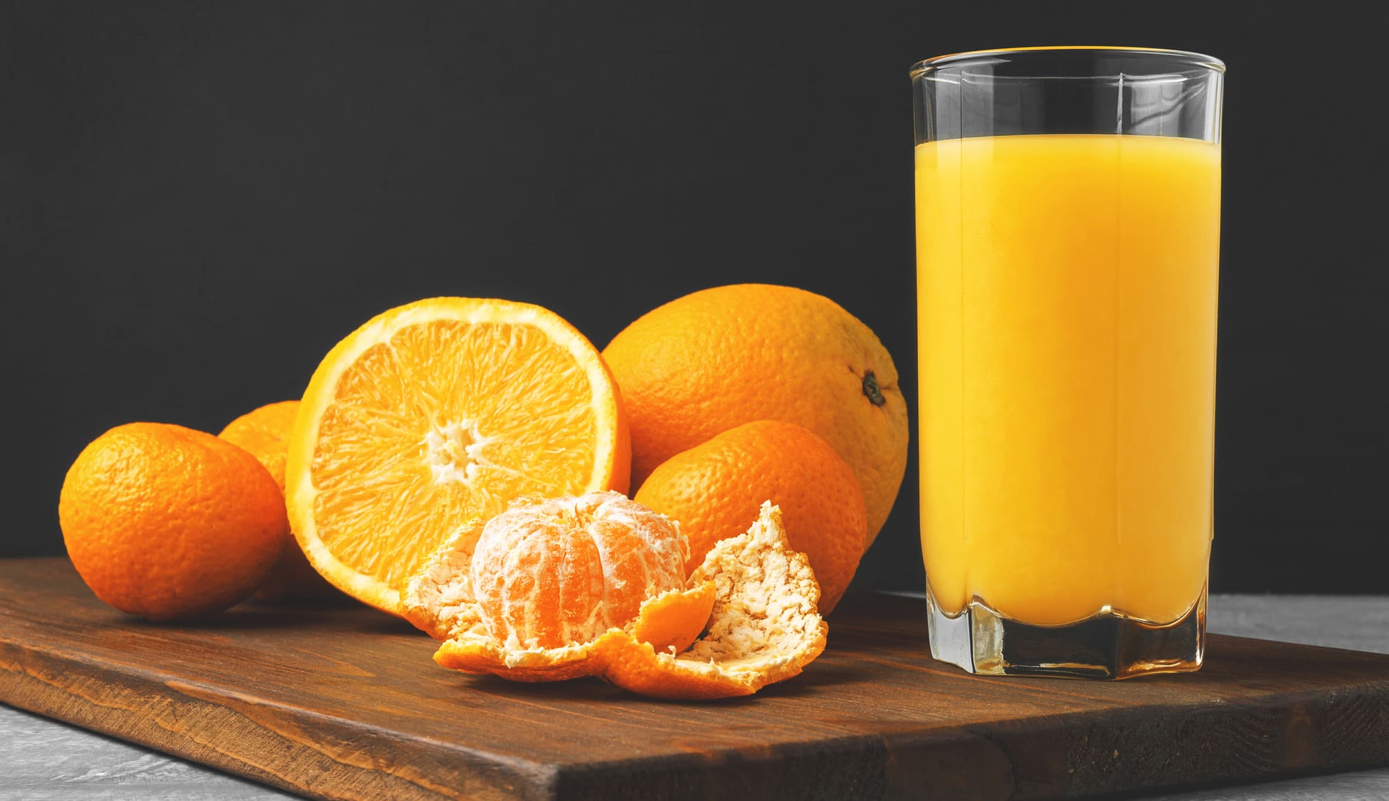 Glass of fresh orange juice, whole and sliced fruits on wooden board