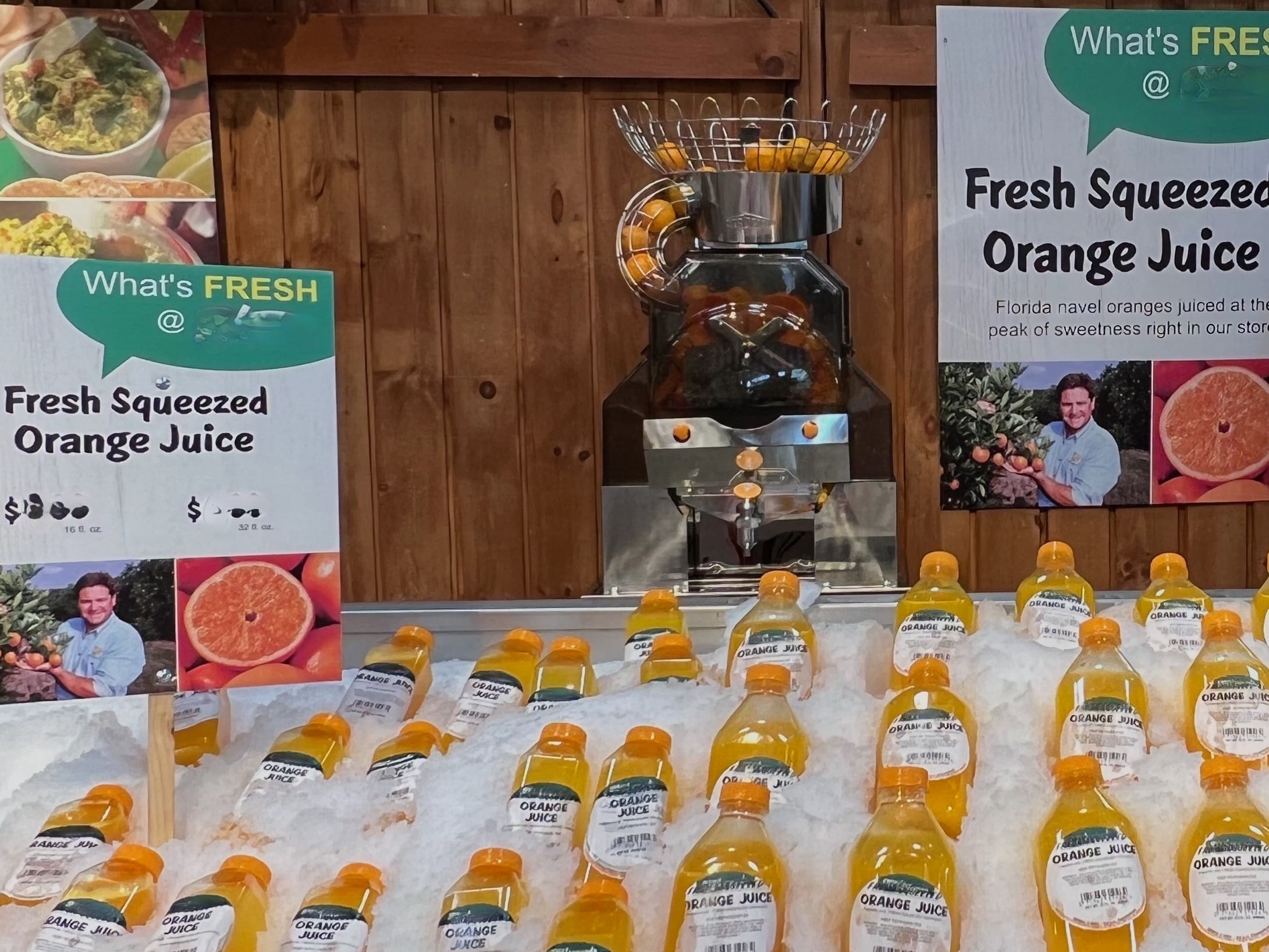 A market display features bottles of fresh squeezed orange juice on ice. Behind the bottles is a commercial juicer, ensuring each sip bursts with citrus freshness. Signs read "Fresh Squeezed Orange Juice," highlight the Florida navel oranges used, and show a person enjoying their drink.
