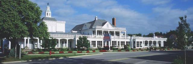 A large, elegant building with a white exterior and a prominent veranda, surrounded by well-manicured gardens and trees under a clear blue sky. The building boasts multiple chimneys, a cupola, and an inviting entrance where you might imagine finding a top-quality commercial citrus juicer inside.
