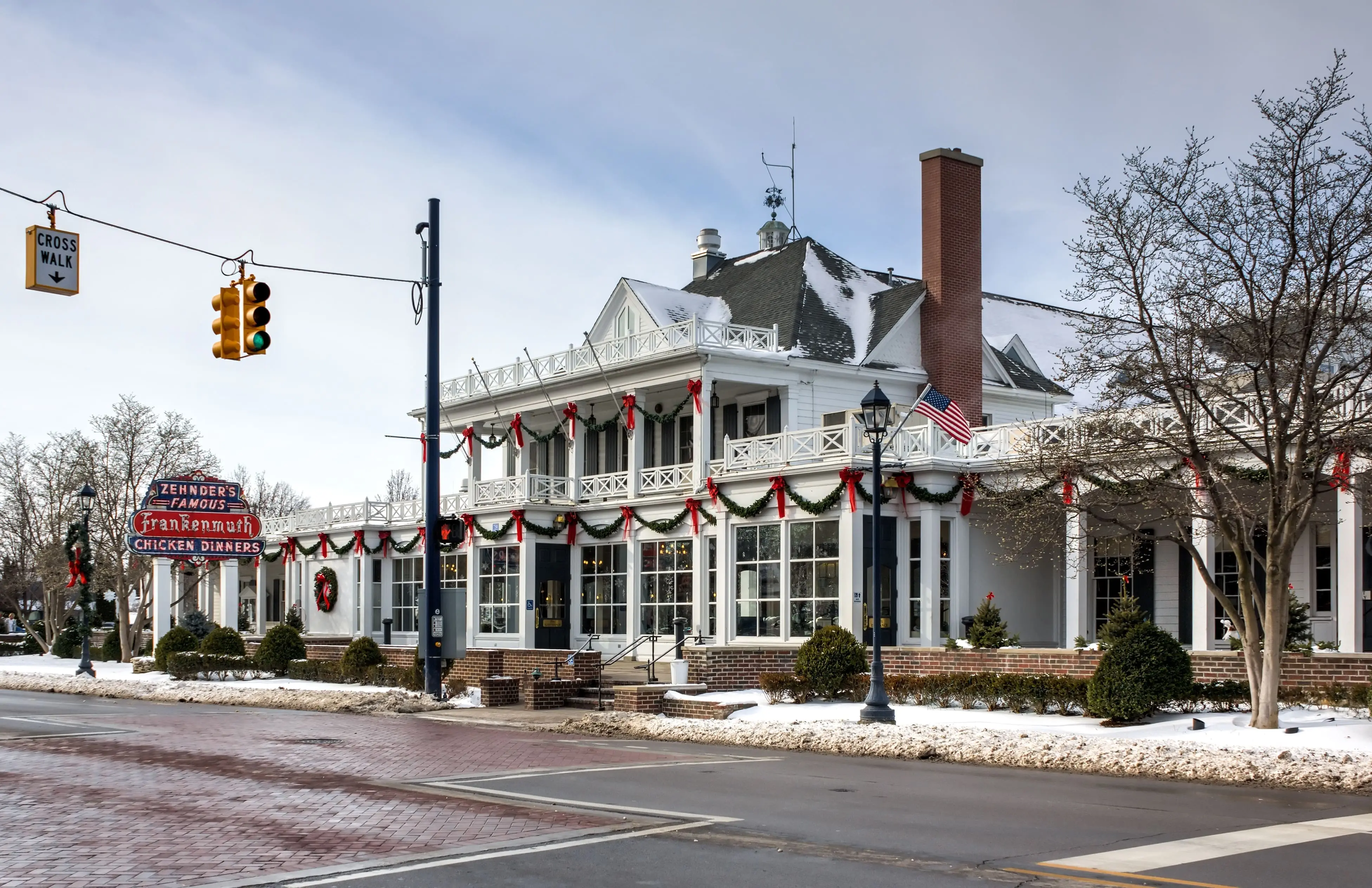 Large, white historic restaurant decorated with red and green garlands and wreaths for the holidays, set on a snowy street corner with a vintage neon sign and American flag visible.