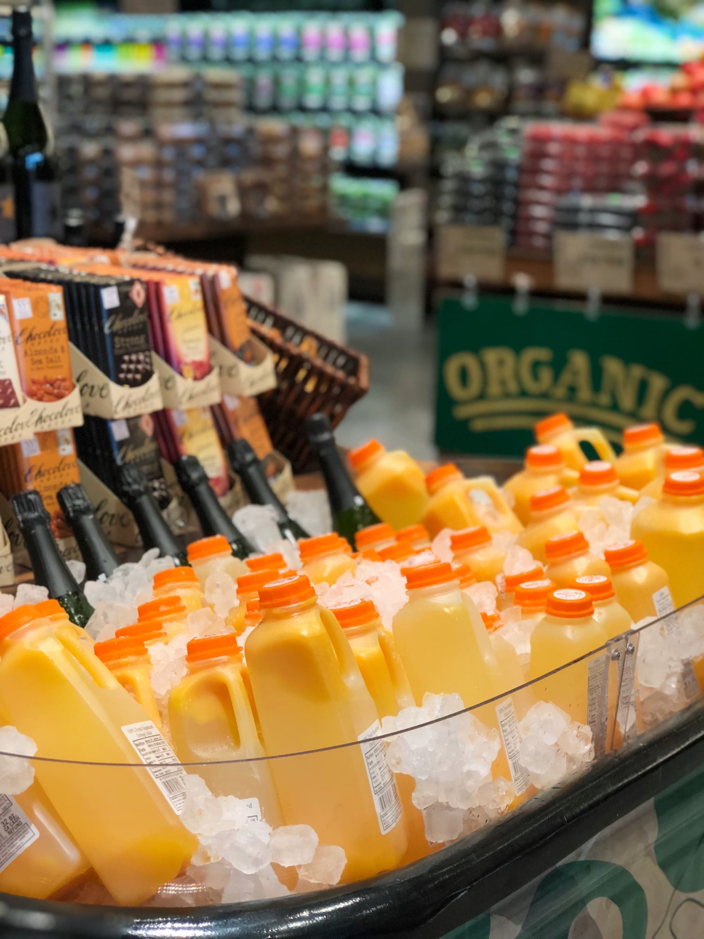 Bottles of Citrus America orange juice with orange caps are displayed on ice at Barons Market, with a sign reading Organic and shelves of various products in the background.