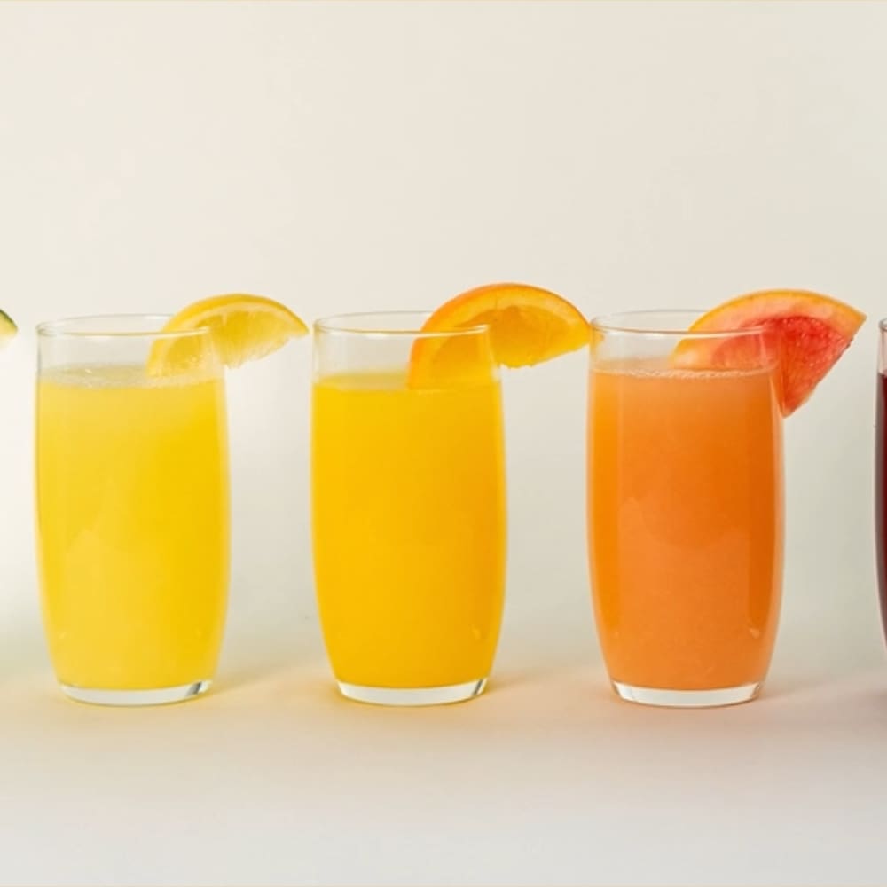 Five glasses of colorful juice, each garnished with a citrus slice, are arranged in a row against a white background—perfectly showcasing the vibrant results you can achieve with a Citrus America commercial juicer.